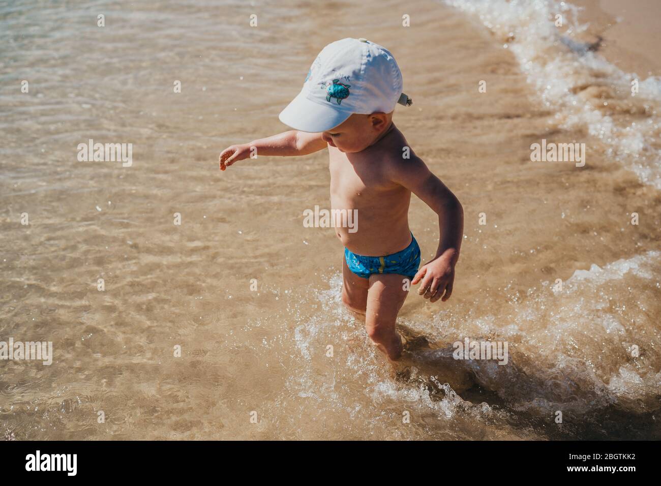 Junge, die an einem sonnigen Urlaubstag ins Wasser am Strand gehen Stockfoto