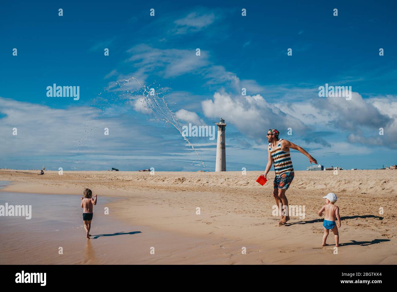 Kinder spielen mit Wasser am Strand mit ihrem Vater an einem sonnigen Tag Stockfoto