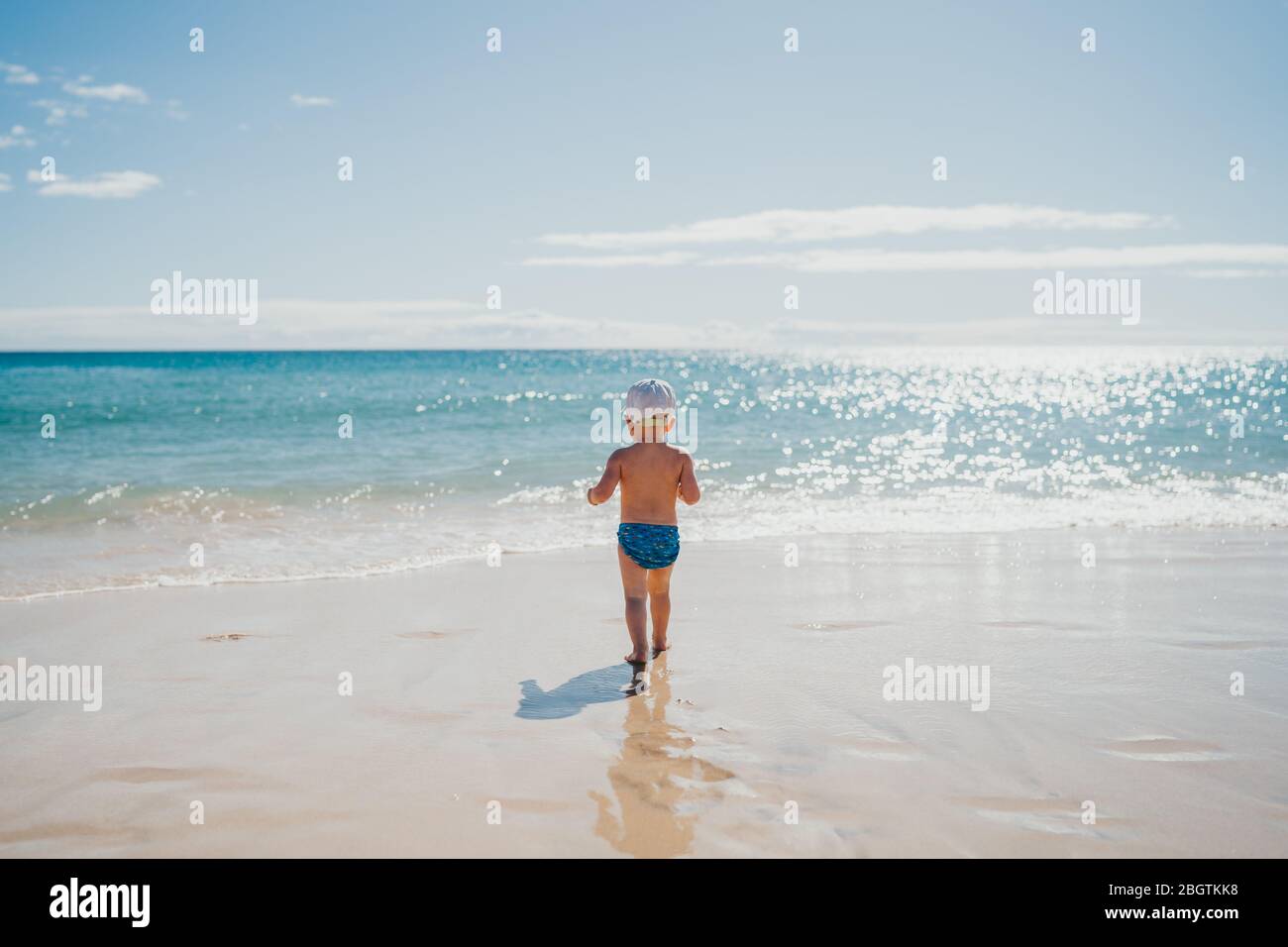 Junge, die an einem sonnigen Urlaubstag ins Wasser am Strand gehen Stockfoto