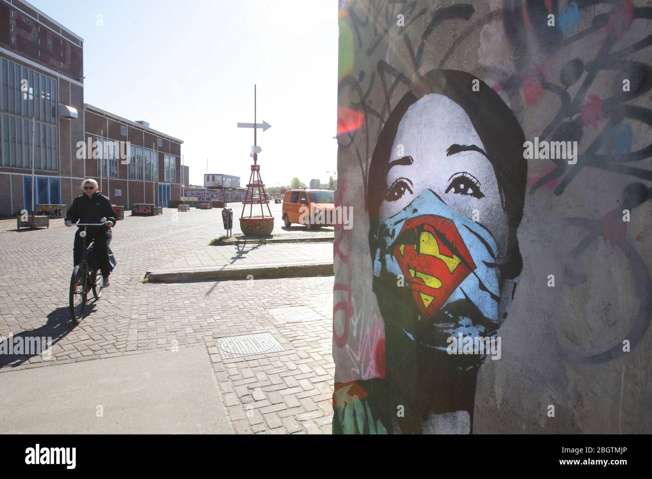 Eine Frau fährt mit dem Fahrrad in der Nähe eines Wandbildes 'Super Nurse' des Künstlers FAKE am 21. April 2020 in Amsterdam, Niederlande. Street Art an einer Wand des ehemaligen NDS Stockfoto