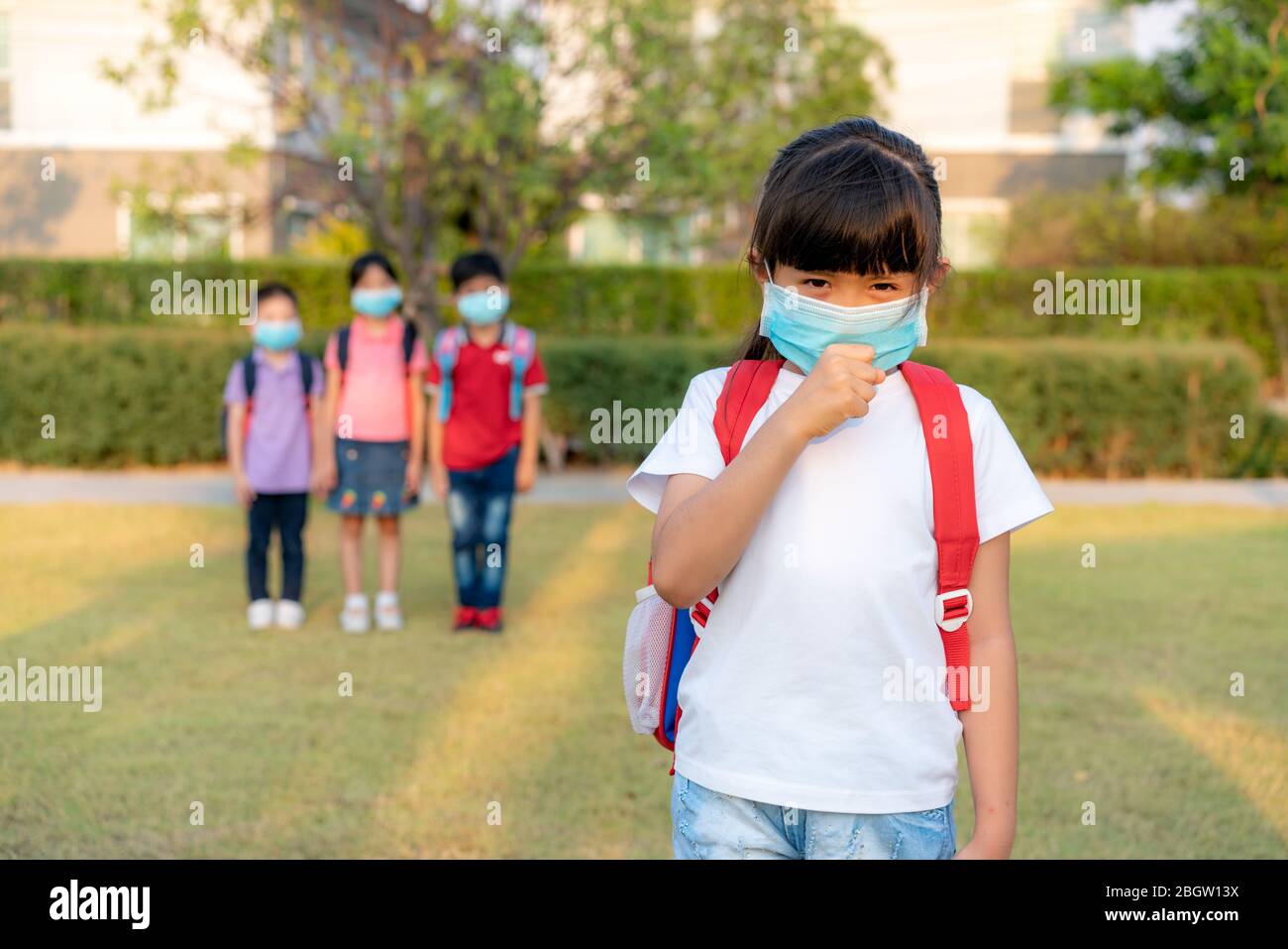 Asiatische Mädchen Vorschule Kind Student trägt gesunde Gesichtsmaske niesen mit Freunden im Hintergrund. WER empfiehlt mindestens 6 Füßlinge Abstand zwischen yo Stockfoto