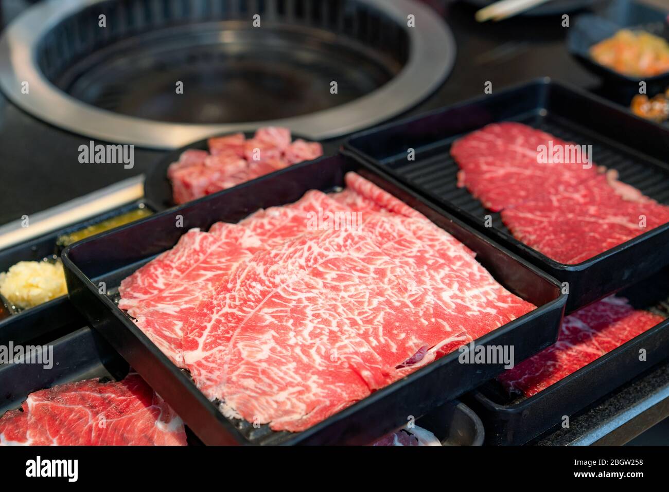 Teller mit rohem Fleisch wie Premium Qualität rohes geschnittenes Wagyu-Rind, Schweinefleisch, Sushi und Dip-Sauce. Auch für den traditionellen japanischen Grill vorbereitet Stockfoto