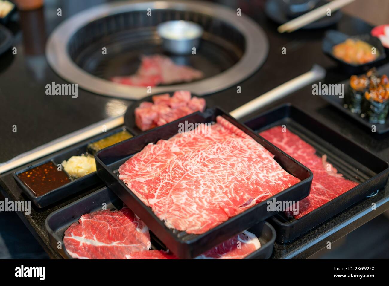 Teller mit rohem Fleisch wie Premium Qualität rohes geschnittenes Wagyu-Rind, Schweinefleisch, Sushi und Dip-Sauce. Auch für den traditionellen japanischen Grill vorbereitet Stockfoto
