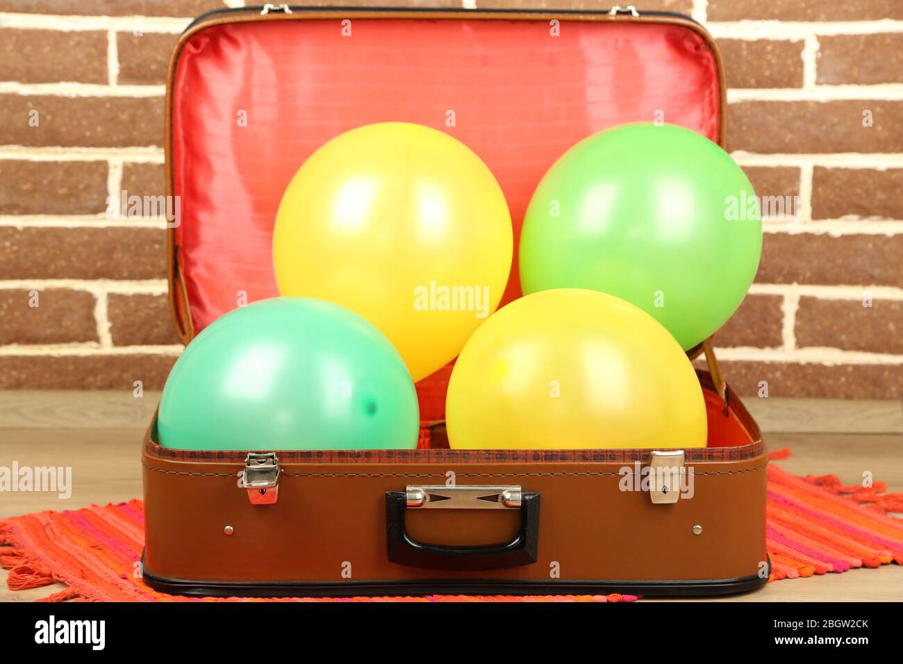 Haufen von Ballons in verschiedenen Farben in alten Koffer, auf Backstein Wand Hintergrund Stockfoto