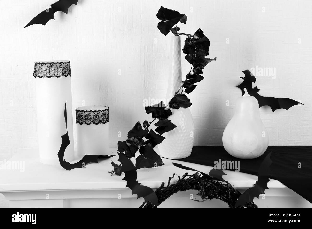 Weiße Kerzen, Pflanzen in Vase und kleinen weißen Kürbis auf Tisch auf weißem Wandhintergrund Stockfoto