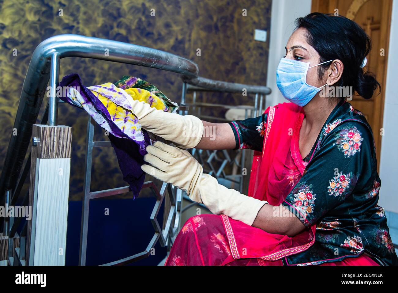 Coronavirus. Indische Frau mit Gesichtsmaske Reinigung und Desinfektion ihres Hauses während Coronavirus-Epidemie. Reinigung Metallgeländer. Vermeidung von COVID- Stockfoto