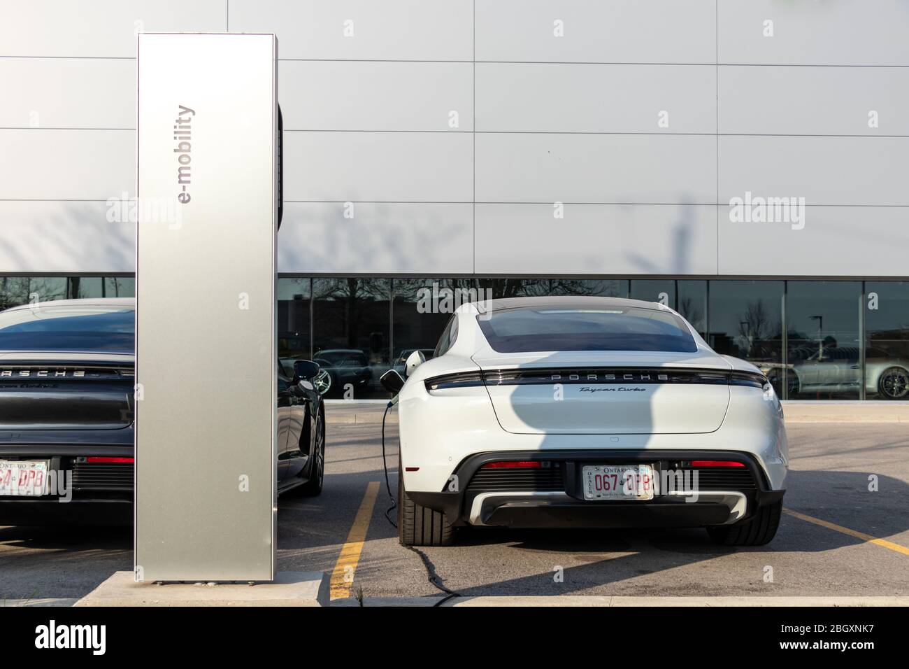 Porsche E-Mobility EV Ladestation in einem Autohaus mit zwei neuen Porsche Taycan’s im Hintergrund. Stockfoto