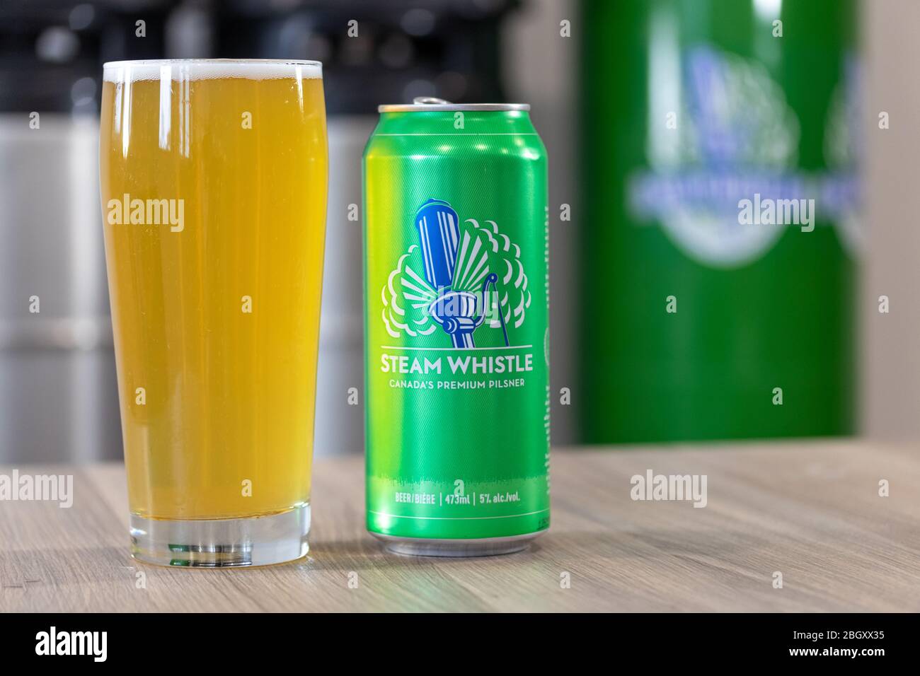 Dampfpfeife Bierkanne mit Bierkiegeln auf einem Tisch neben einem vollen Glas Bier, vor gestapelten Fässern. Stockfoto