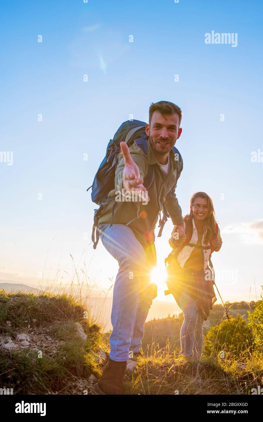 Menschen helfen sich gegenseitig, bei Sonnenaufgang einen Berg hinauf zu wandern. Stockfoto