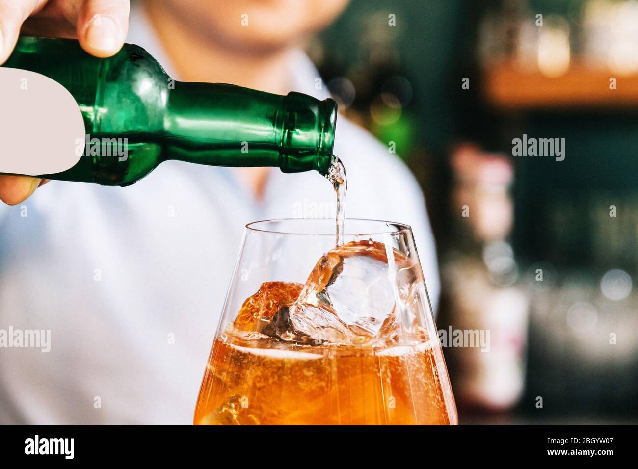 Bild der Ernte Mixologe gießt Alkohol auf die orange fruchtigen Cocktail, die mit in Scheiben geschnittenen Orange in einem Weinglas mischen. Stockfoto