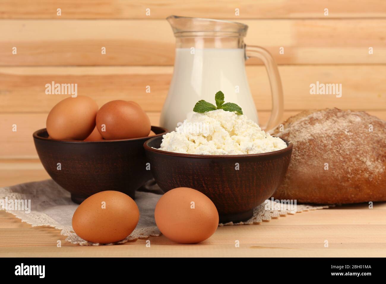 Quark in Tonschüssel mit Krug Milch, Brot und Eier auf Holzplanken Hintergrund Stockfoto