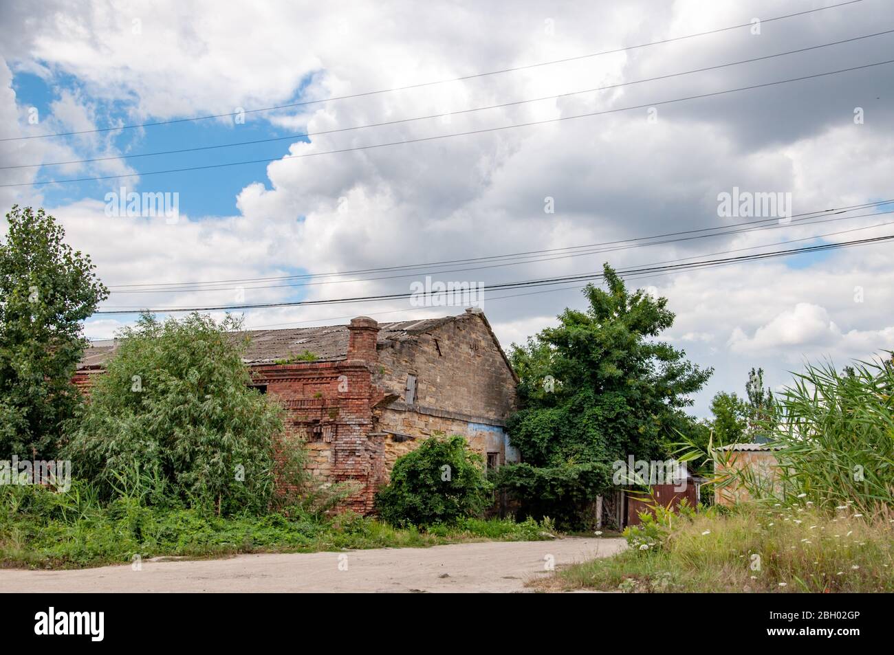 Verlassene Haus mit baufälligen Ziegelmauern, überwuchert von Kletterpflanzen und grünen Bäumen. Wolkiger Himmel über Dorf Szene in der Ukraine Landschaft. Stockfoto