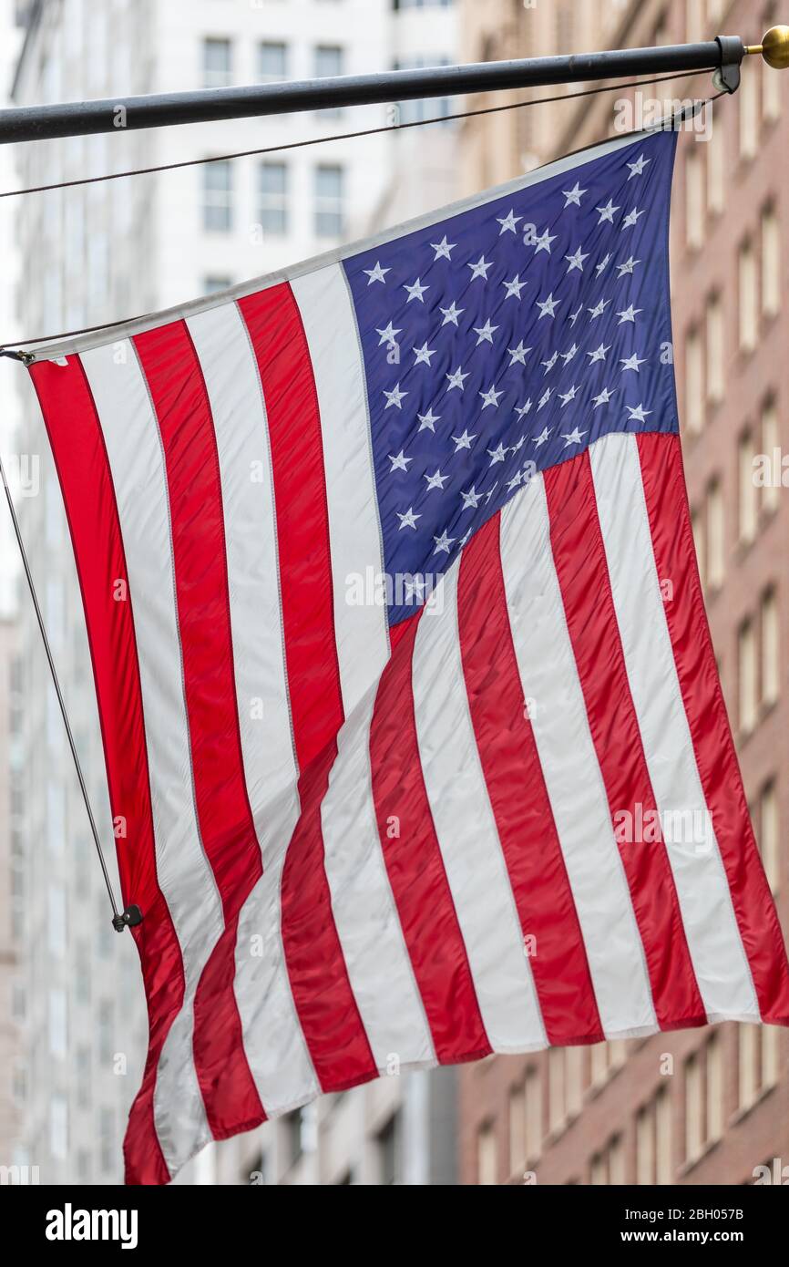 Eine große amerikanische Flagge, die an einer Stange hängt und im Wind winkt; im Hintergrund, unscharf Wolkenkratzer. Stockfoto