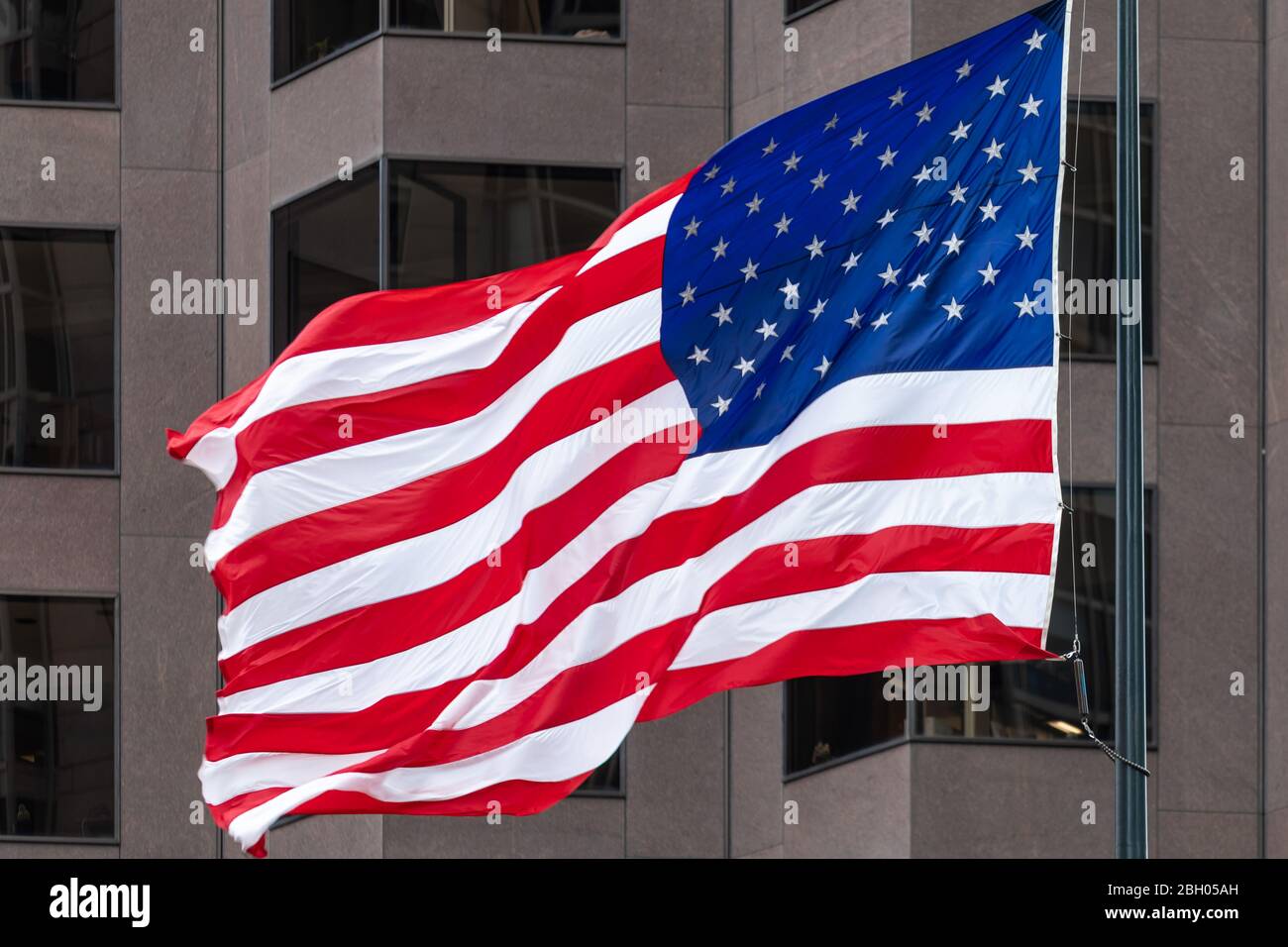 Nahaufnahme einer großen bunten amerikanischen Flagge, die einschwenkt Der Wind gegen die graue geometrische Fassade eines Gebäudes Stockfoto