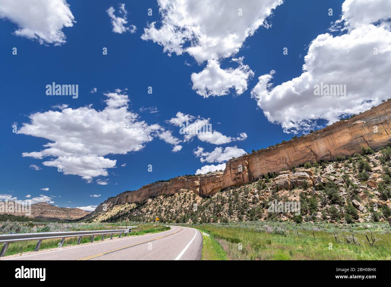 Die Scenic Byway 12 erstreckt sich bis zum Horizont unter einem blauen Himmel mit geschwollenen Wolken, und flankiert von einem Kamm aus rotem Sandstein Stockfoto