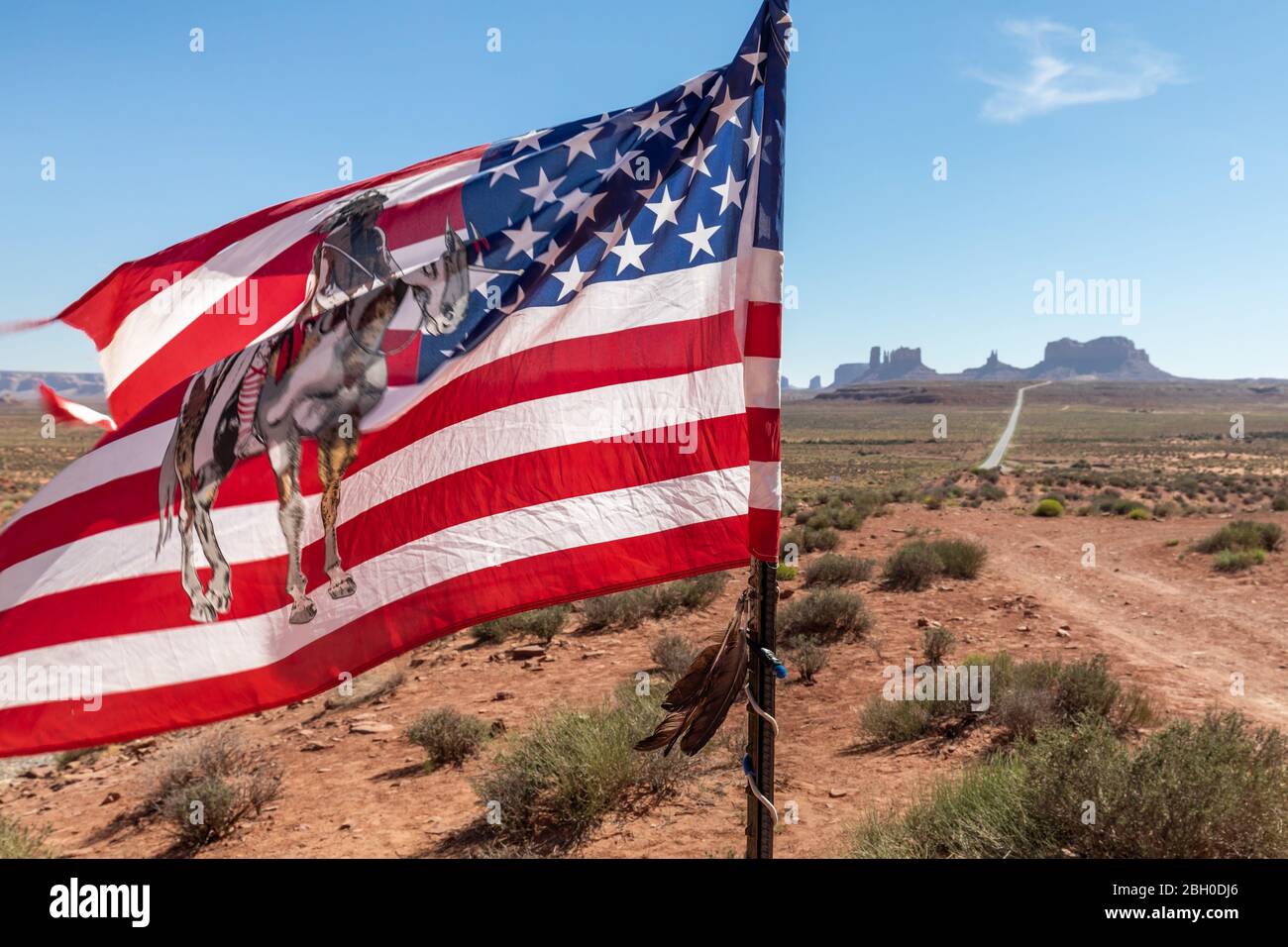Die indianische Flagge winkt im Wind, mit einer langen Straße, die sich bis zum Monument Valley im Hintergrund erstreckt Stockfoto