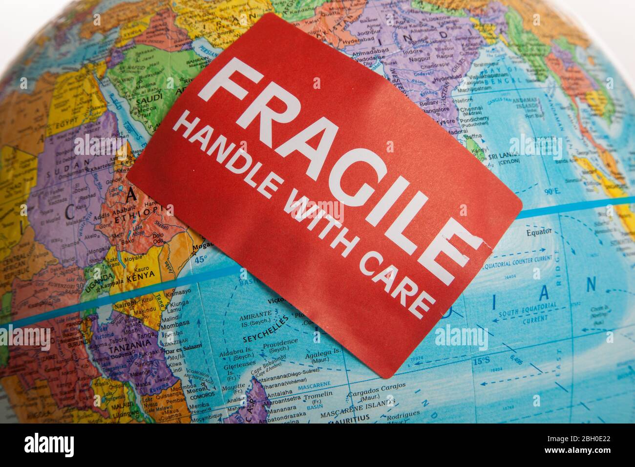 Eine Erdkugel mit einer zerbrechlichen Hand mit Pflegeaufkleber Stockfoto