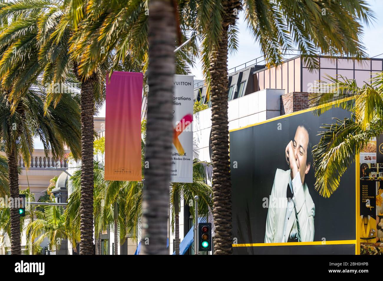 Nahaufnahme eines Teils des Rodeo Drive, mit einer Reihe von Palmen im Vordergrund und einer Werbung im Hintergrund Stockfoto