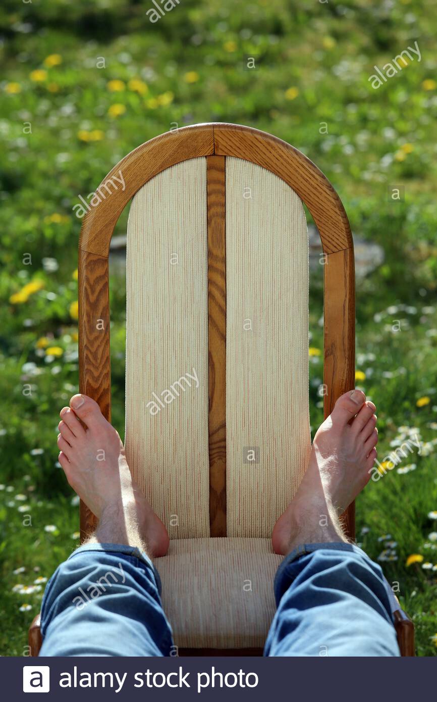 Die Füße eines jungen Mannes, der sich auf einem Stuhl im Sonnenschein im Frühling in einem Garten entspannt. Stockfoto