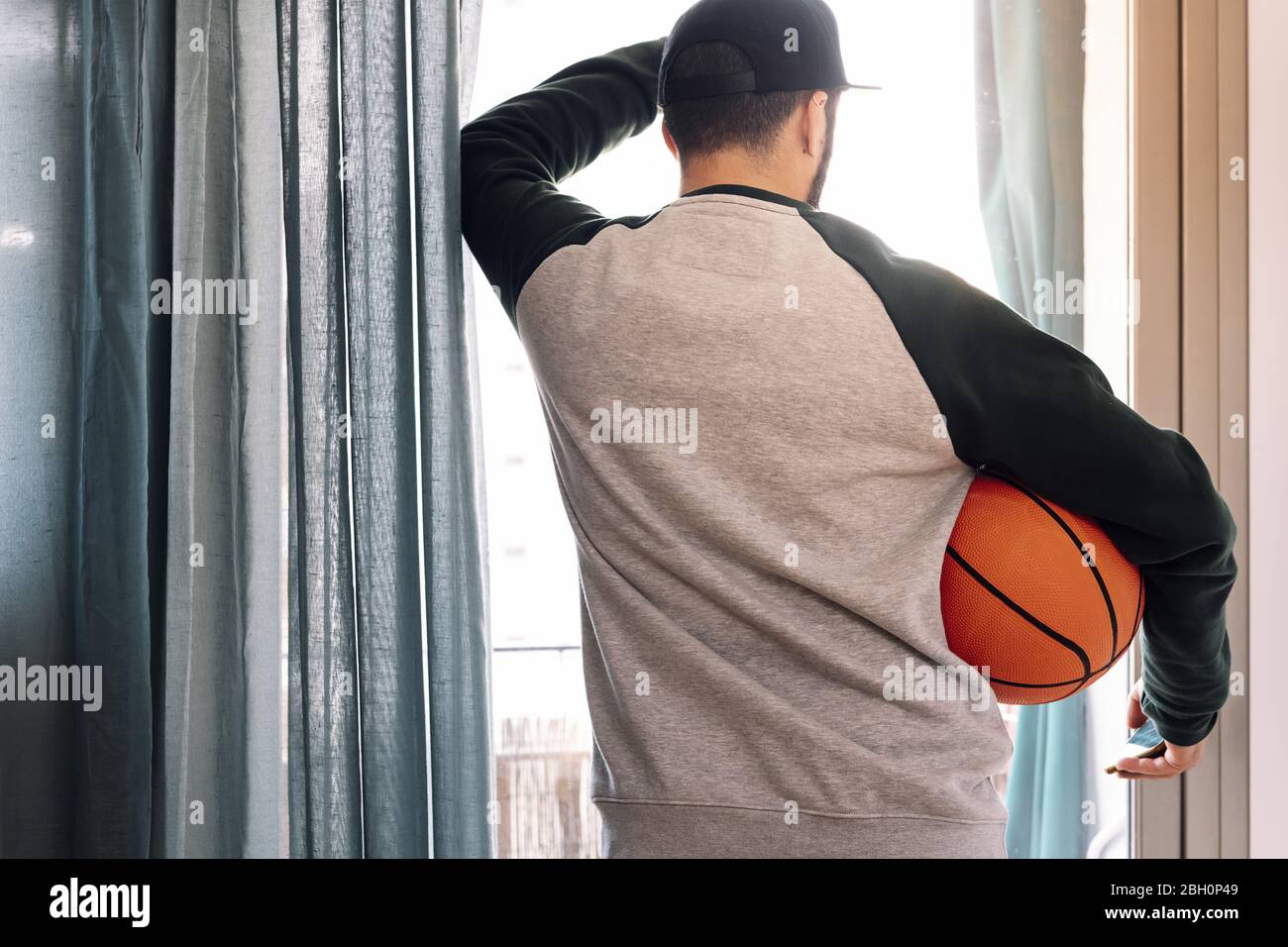 Mann beschränkt Blick aus seinem Fenster mit einem Basketball, Konzept der Quarantäne und Einsperrungen Stockfoto