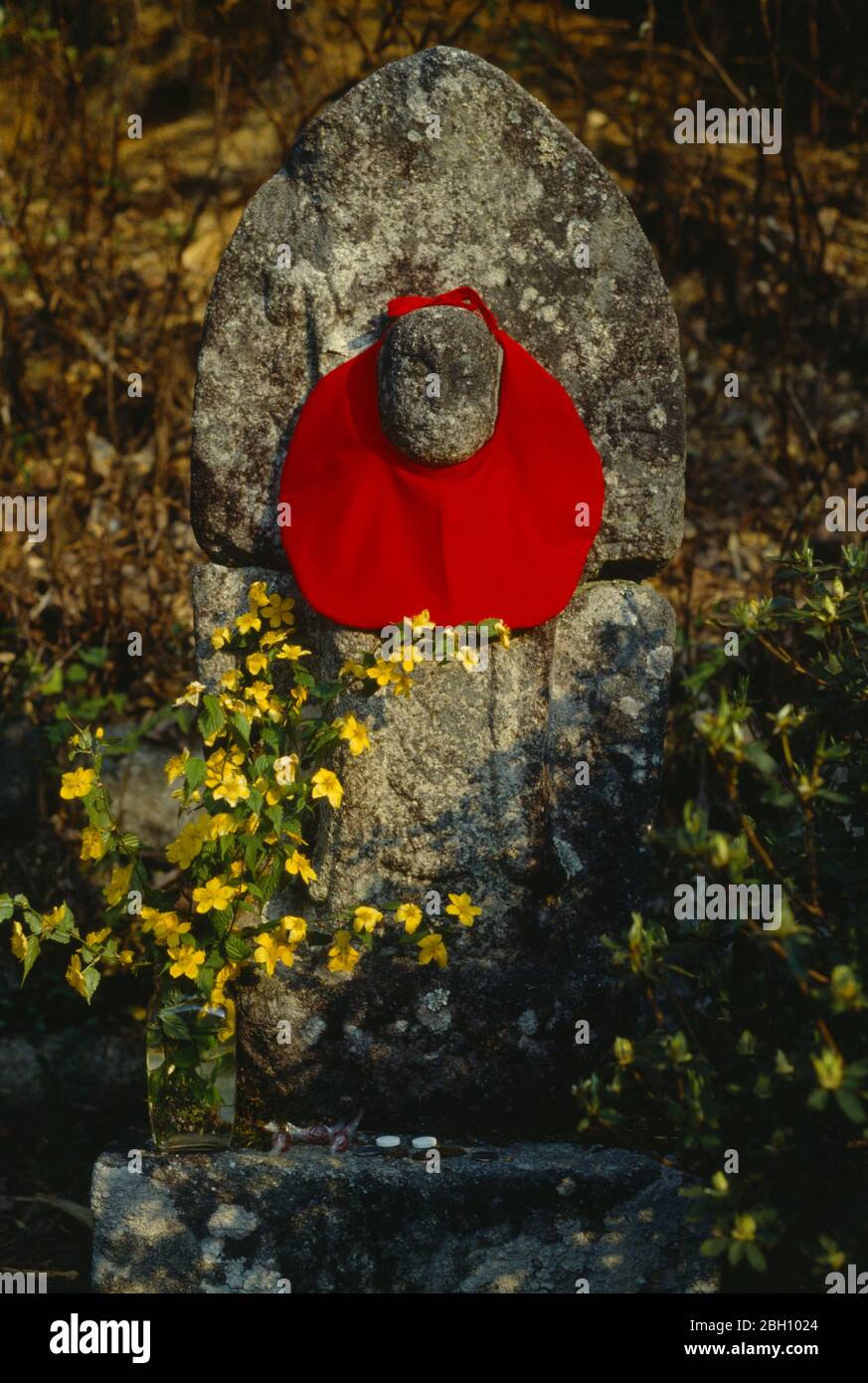 Japan, Religion, Straßengedenken mit rotem Tuch um Steinstruktur und Vase  mit gelben Blumen gebunden Stockfotografie - Alamy