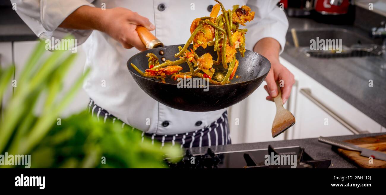 Ein Koch bereitet nepalesische Gerichte in einer Küche zu. Hühnchen und Gemüse werden in die Luft geworfen Stockfoto