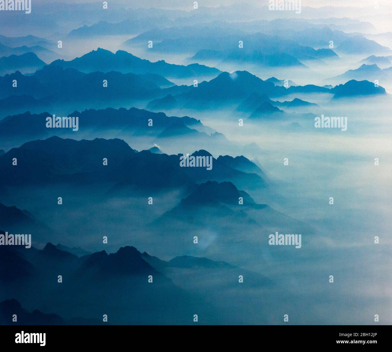 Aus Wolken und Nebel erheben sich die silhouettierten Berggipfel der europäischen Alpen, wie aus einem Flugzeug gesehen Stockfoto