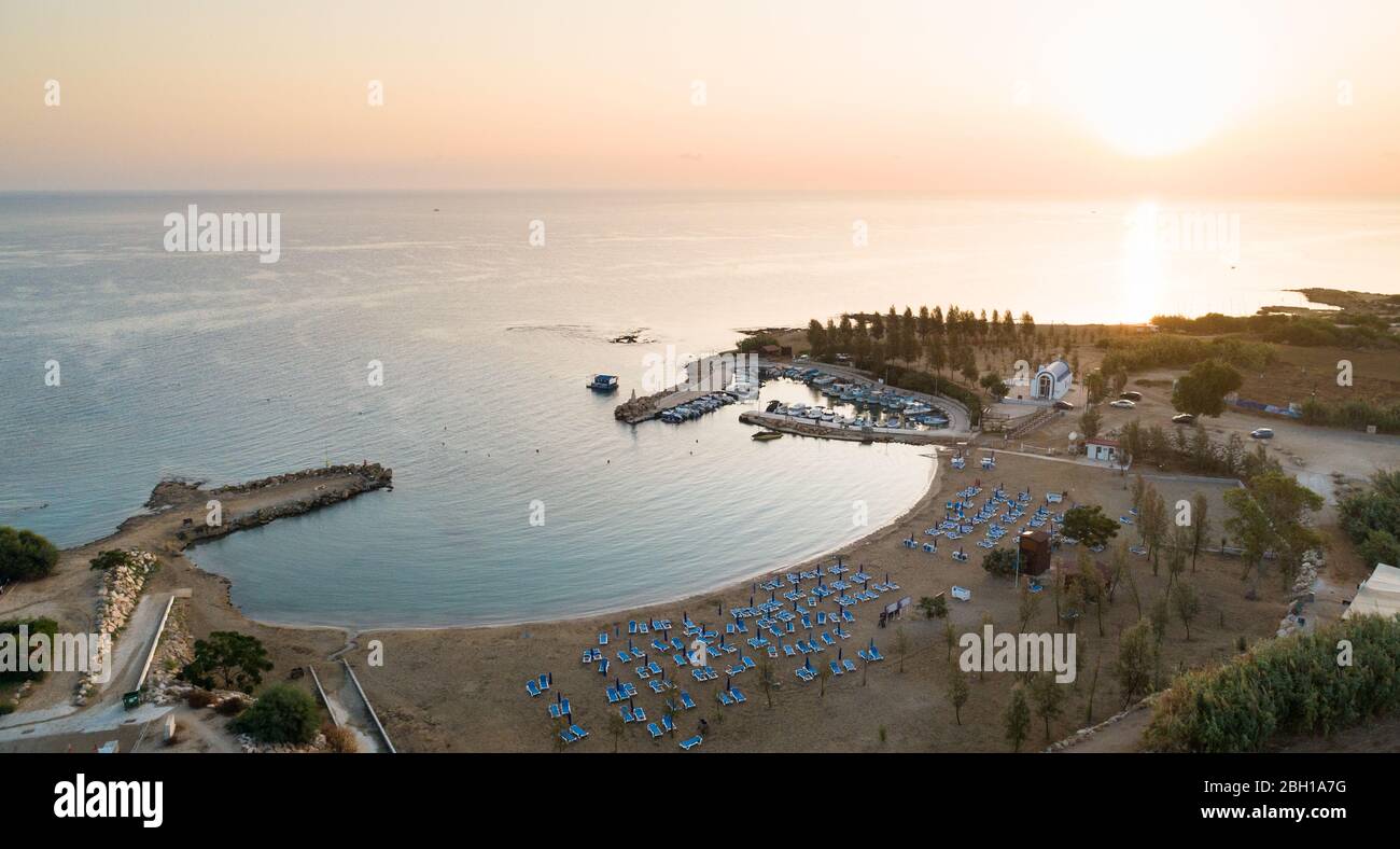 Luftbild des Sonnenuntergangs an der Küste und die weiße, gewaschene Kapelle am Strand Agia Triada, Protaras, Famagusta, Zypern von oben. Vogelperspektive auf Tour Stockfoto