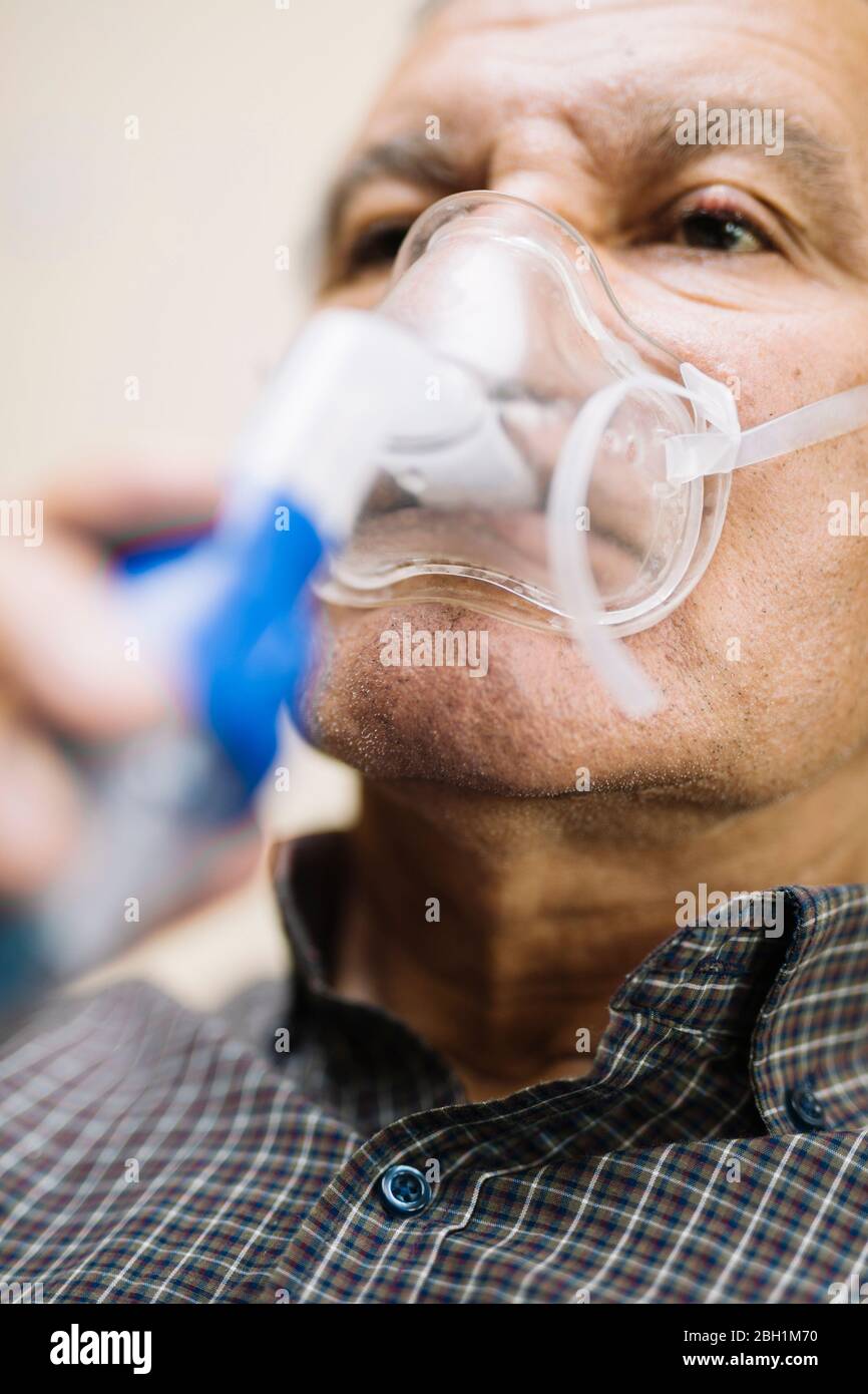 Leitender Mann, der medizinische Geräte für die Inhalation mit Atemschutzmaske verwendet, Vernebler im Zimmer Stockfoto