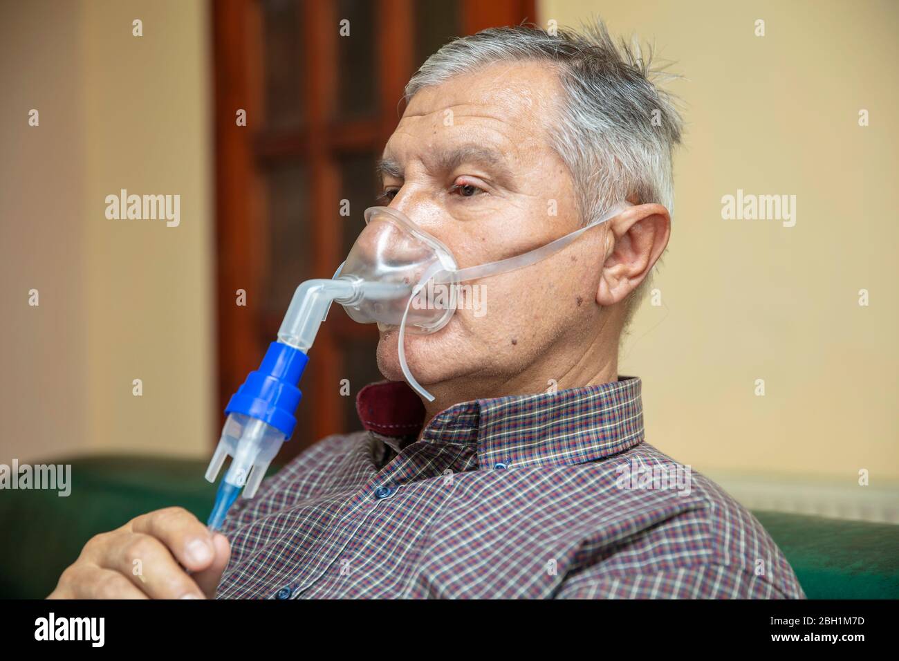 Leitender Mann, der medizinische Geräte für die Inhalation mit Atemschutzmaske verwendet, Vernebler im Zimmer Stockfoto