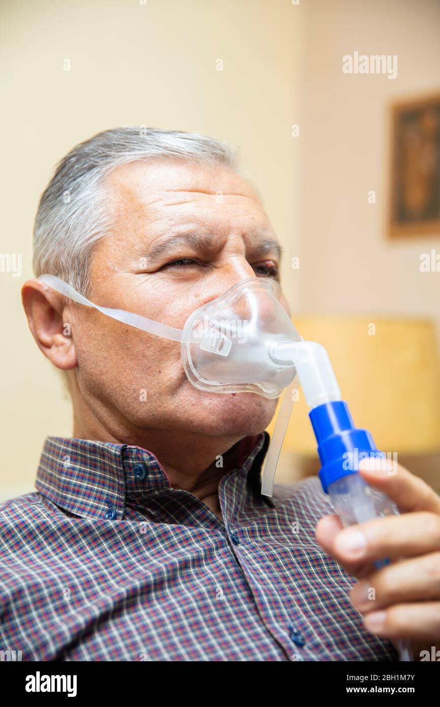 Leitender Mann, der medizinische Geräte für die Inhalation mit Atemschutzmaske verwendet, Vernebler im Zimmer Stockfoto