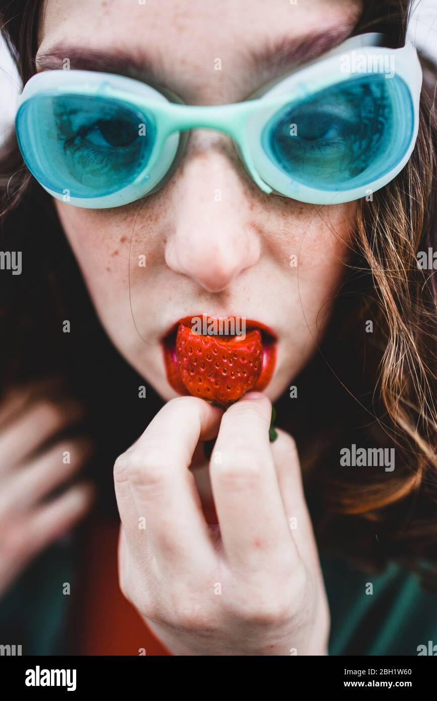 Portrait einer Frau mit blauer Taucherbrille, die Erdbeere frisst Stockfoto