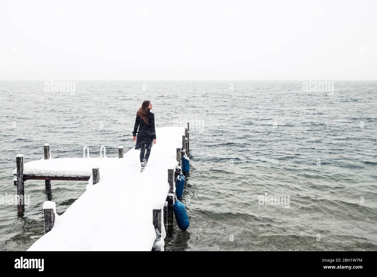 Rückansicht einer jungen Frau, die auf dem verschneiten Steg am Starnberger See läuft Stockfoto