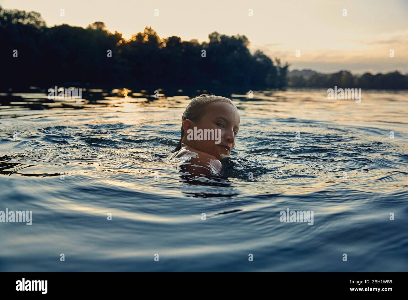 Mädchen, das in der Abenddämmerung in einem See schwimmt Stockfoto