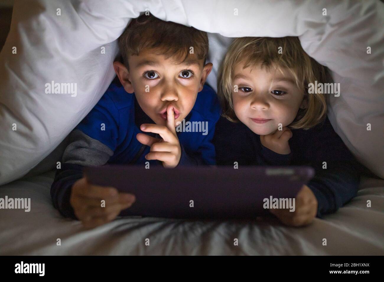 Portrait von Bruder und kleiner Schwester liegen nebeneinander unter einer Decke mit digitalen Tablet Stockfoto