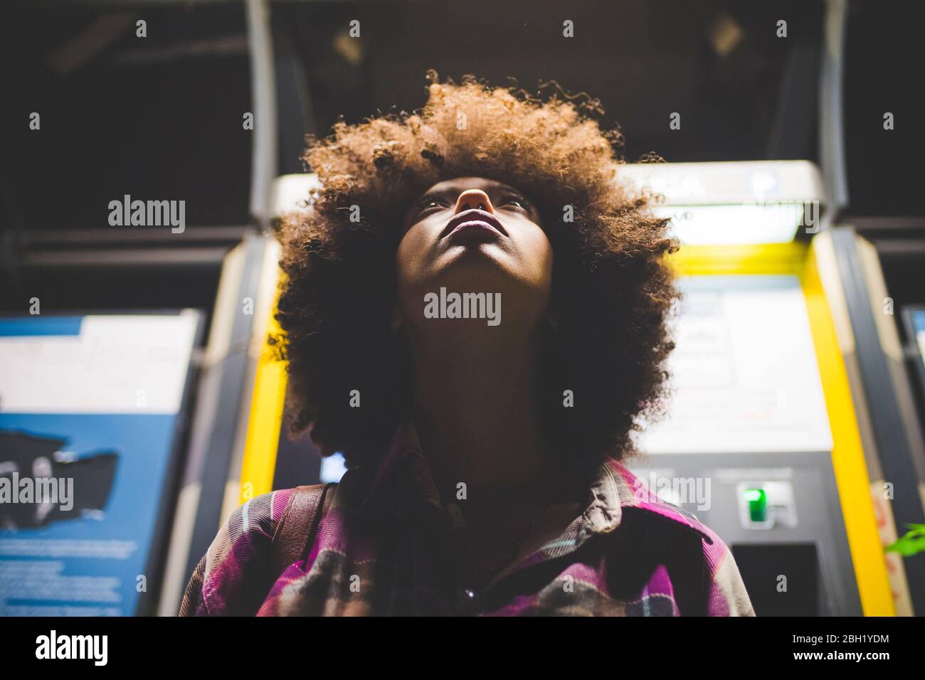 Junge Frau mit afro Frisur am Ticketautomaten in der Nacht suchen nach oben Stockfoto