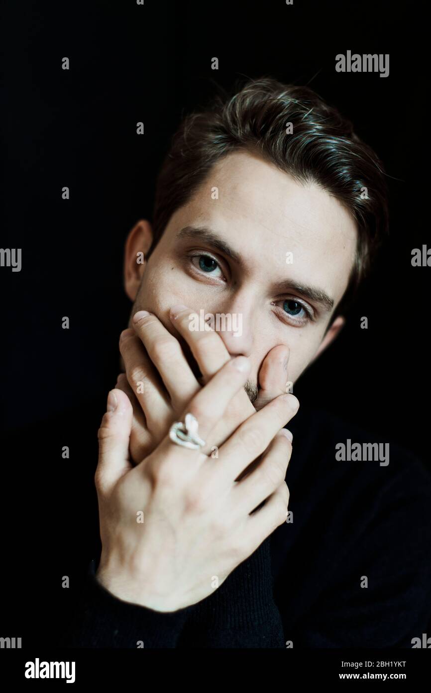 Porträt eines jungen Mannes mit Händen bedeckt Mund vor schwarzem Hintergrund Stockfoto