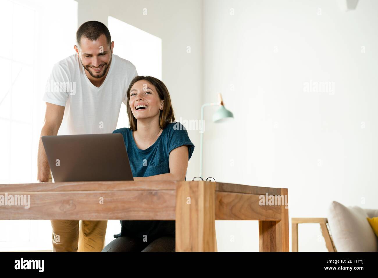 Glückliches Paar, das von zu Hause aus im modernen Wohnzimmer am Laptop arbeitet Stockfoto