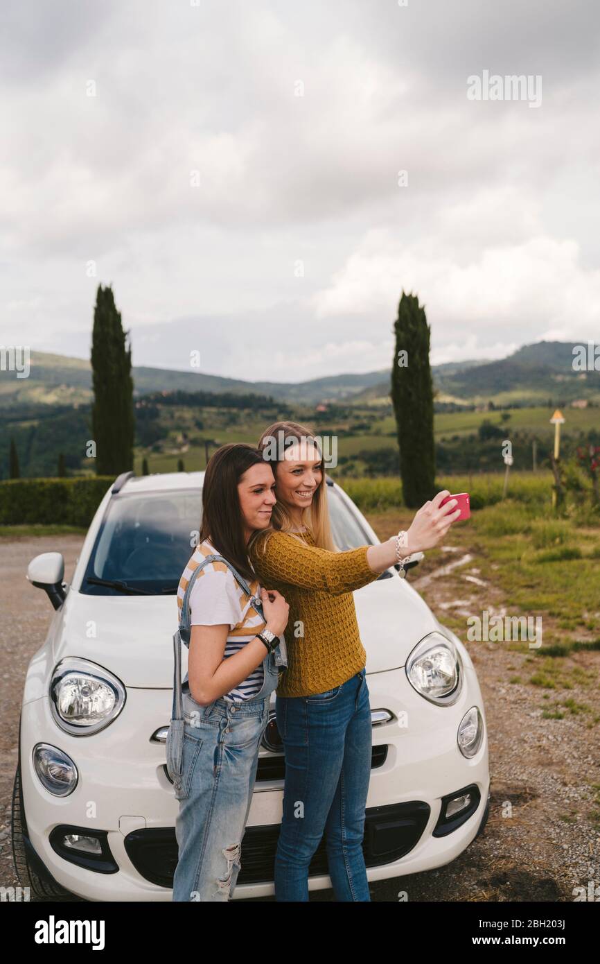 Zwei glückliche junge Frauen stehen neben dem Auto und machen ein Selfie, Toskana, Italien Stockfoto