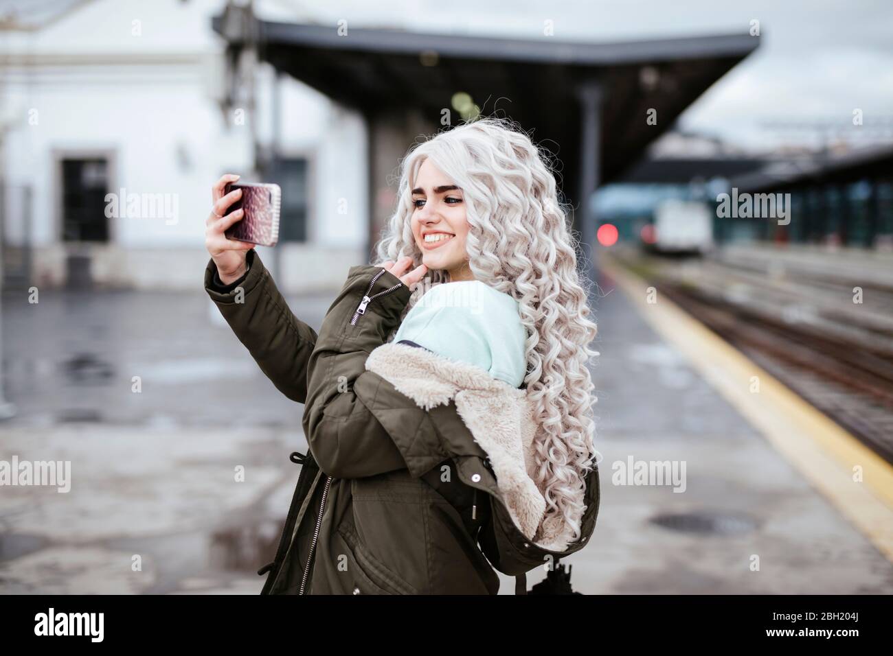 Porträt einer lächelnden jungen Frau, die Selfie mit dem Smartphone auf der Plattform nimmt Stockfoto