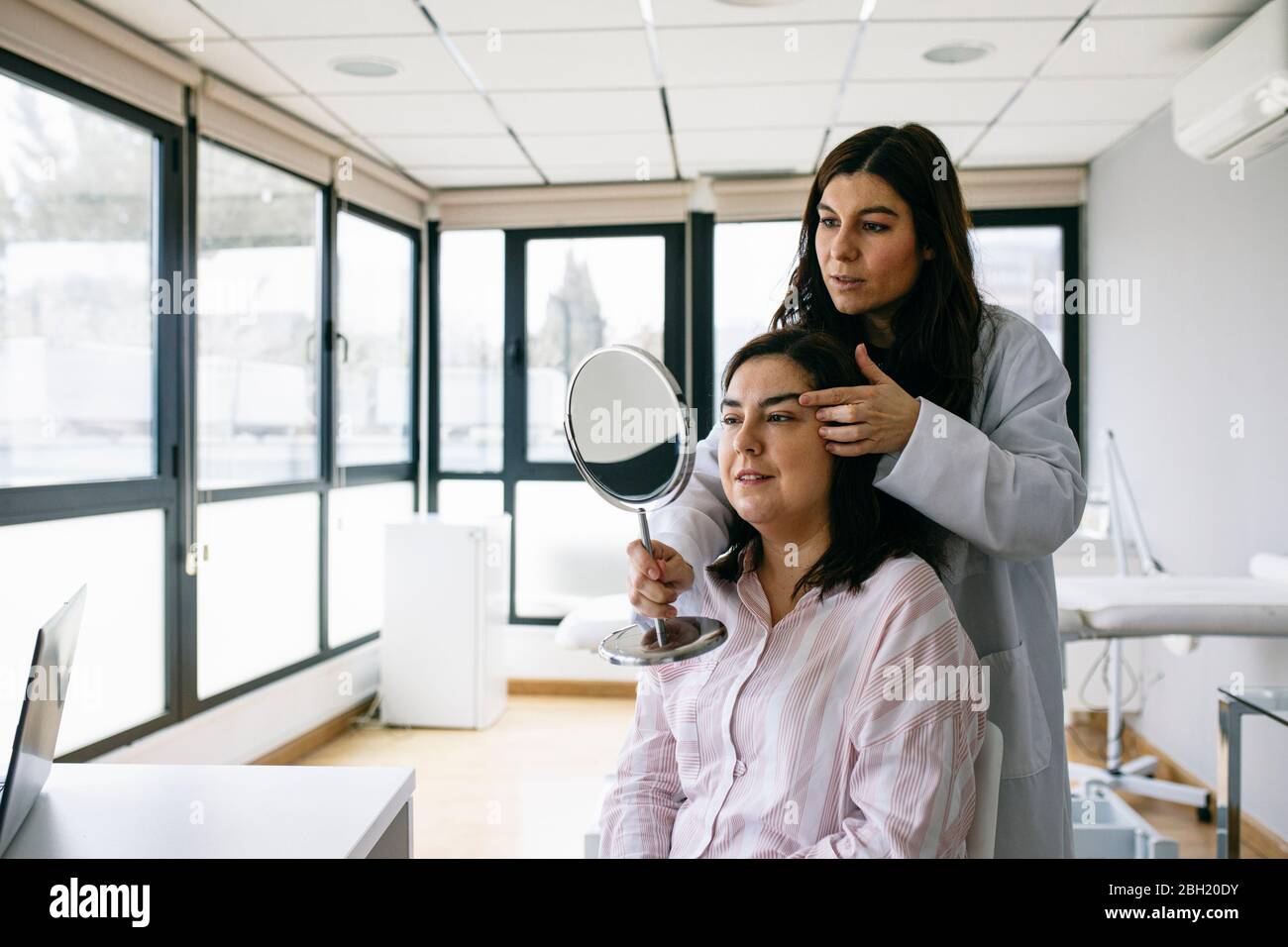 Kosmetischer Chirurg hält Spiegel und sprechen mit dem Patienten in der medizinischen Praxis Stockfoto