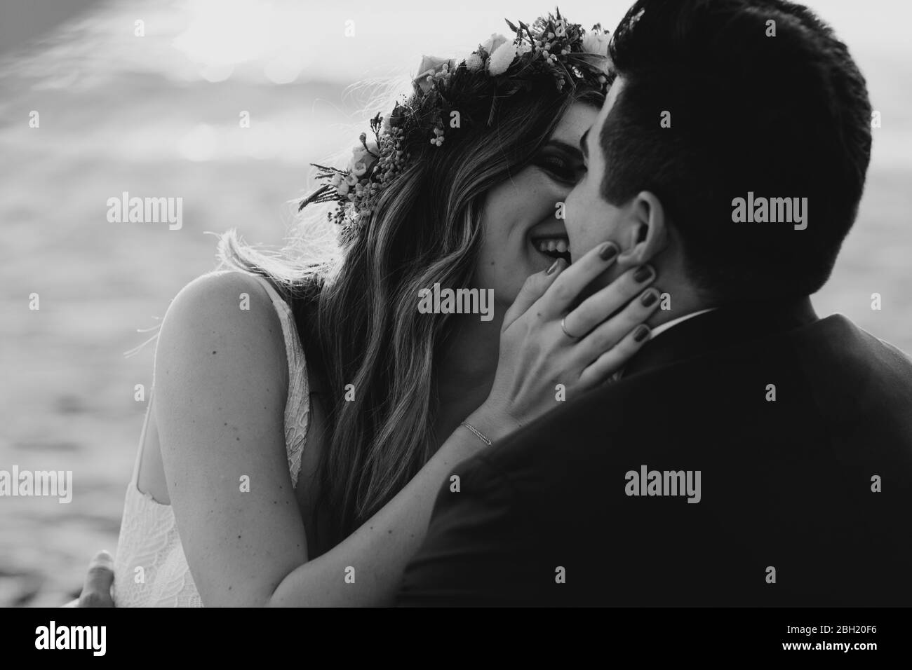 Glückliches Brautpaar küsst sich am Strand, schwarz und weiß Stockfoto