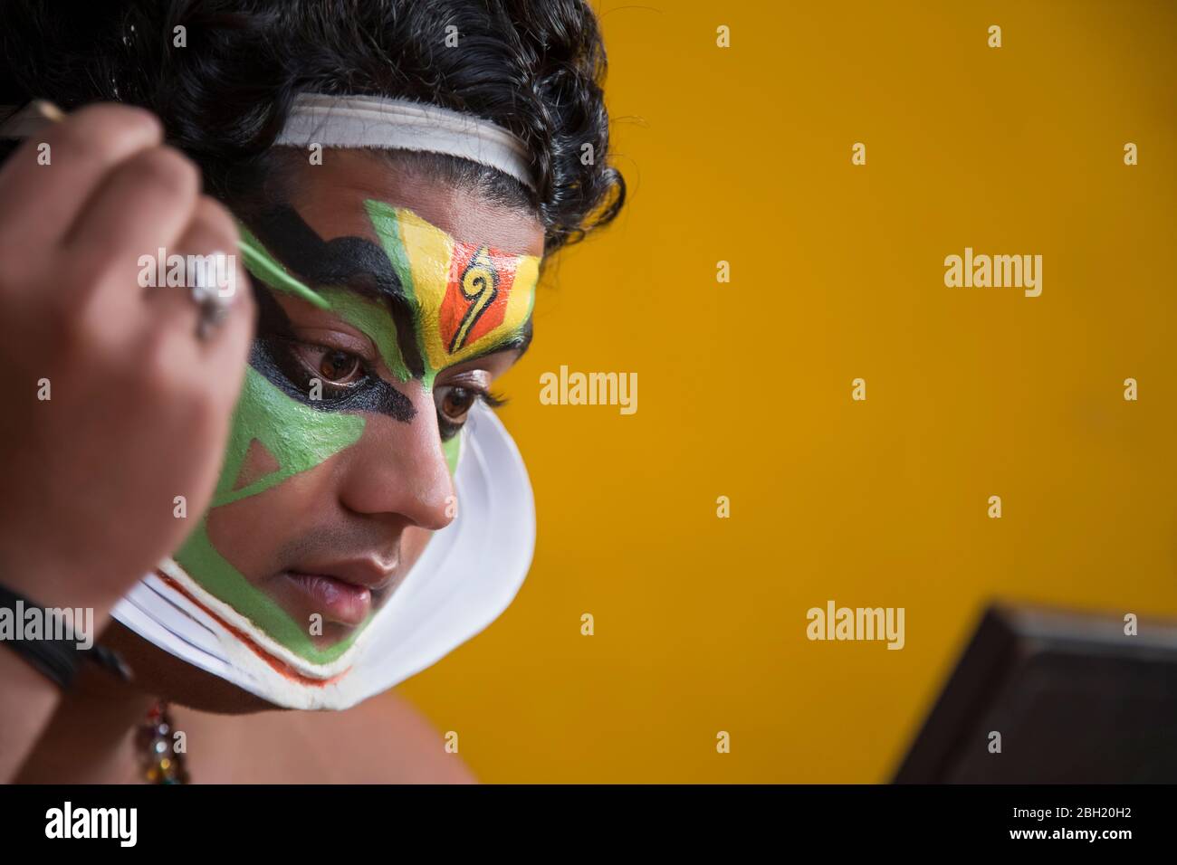 Kathakali Tänzer, der in den Spiegel schaut und grüne Farbe auf sein Gesicht setzt. Stockfoto