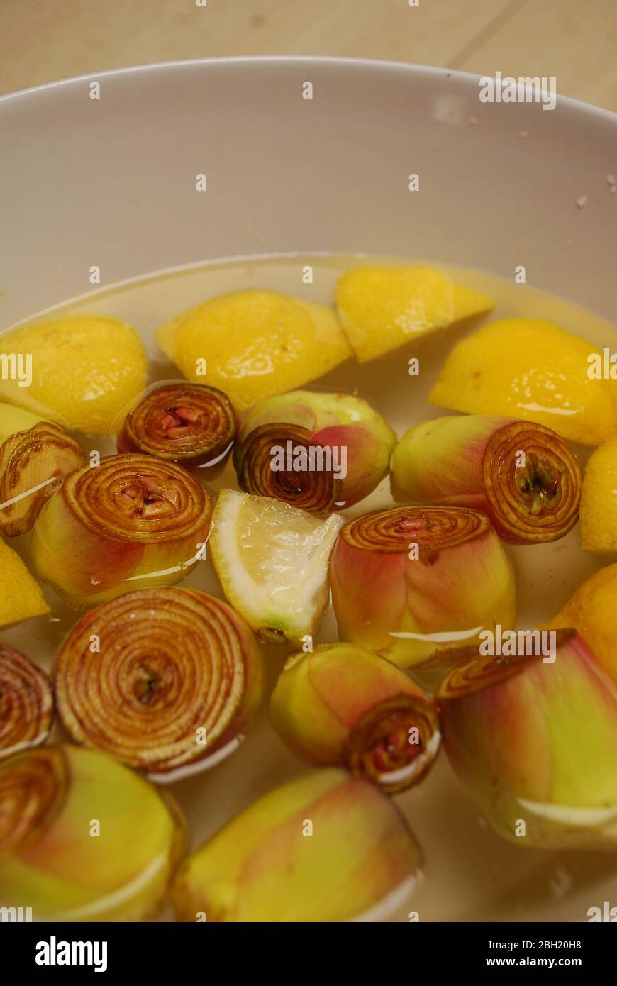 Geschälte italienische Artischocken in einer Schüssel mit Wasser und Zitronen Stockfoto