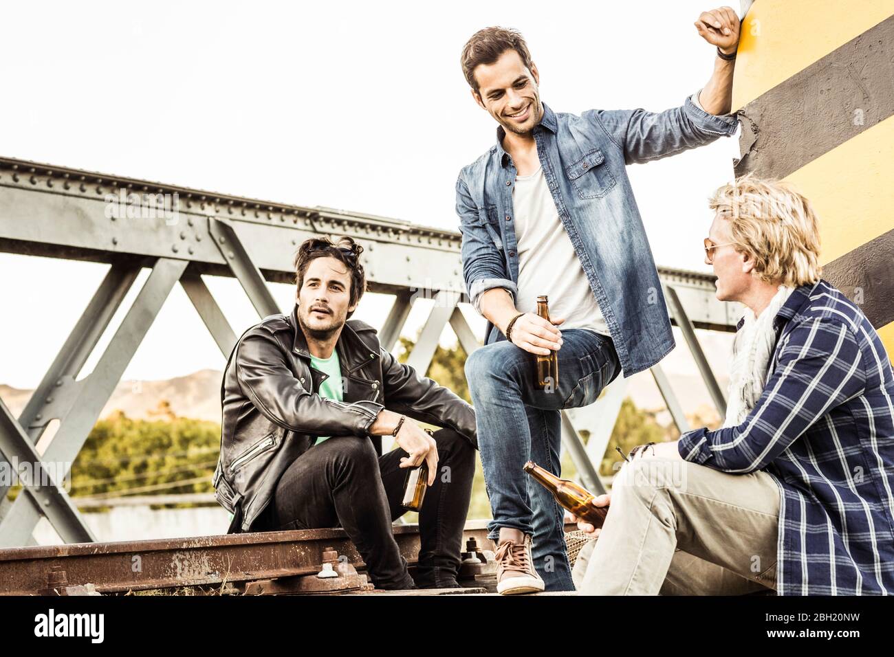 Drei Männer trinken Bier auf einer alten Eisenbahnbrücke Stockfoto