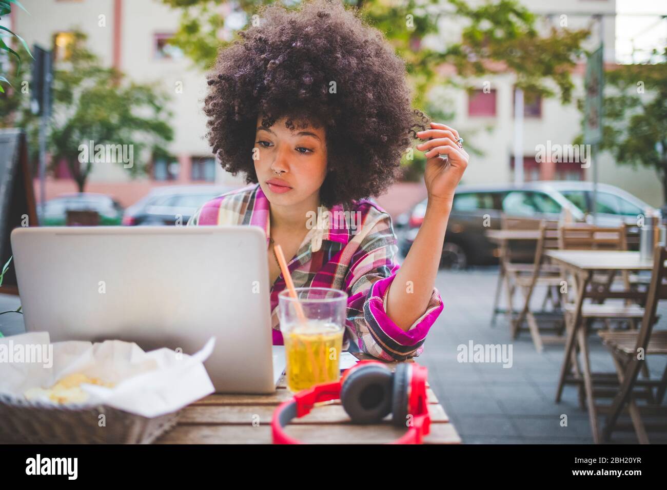 Junge Frau mit Afro-Frisur mit Laptop in einem Café im Freien in der Stadt Stockfoto