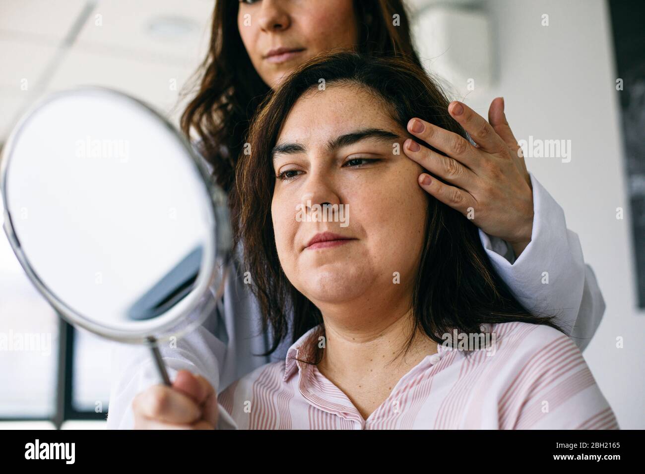 Kosmetischer Chirurg hält Spiegel und sprechen mit dem Patienten in der medizinischen Praxis Stockfoto