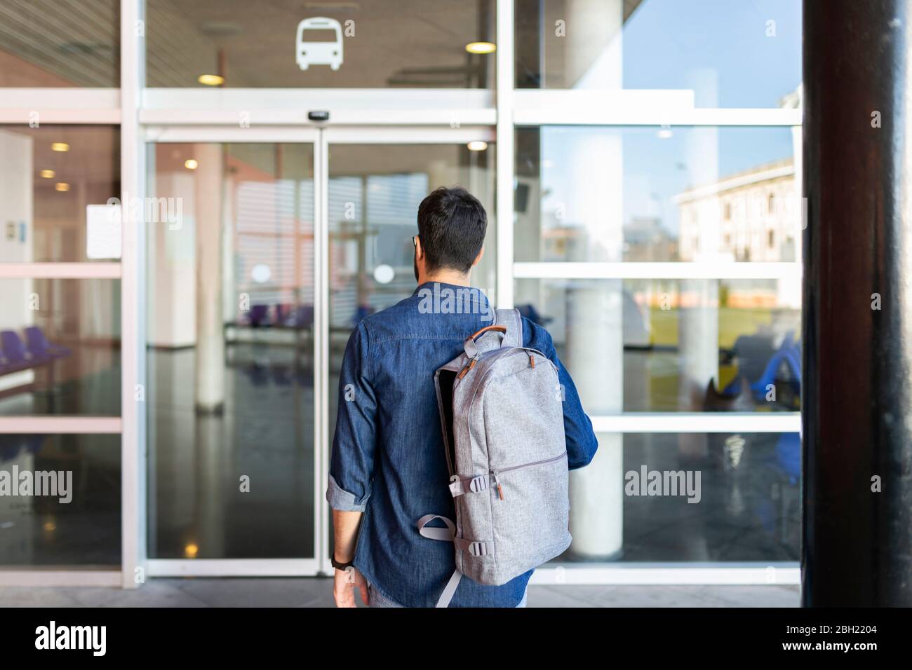 Rückansicht des Mannes mit Rucksack vor dem Eingang der Bushaltestelle Stockfoto