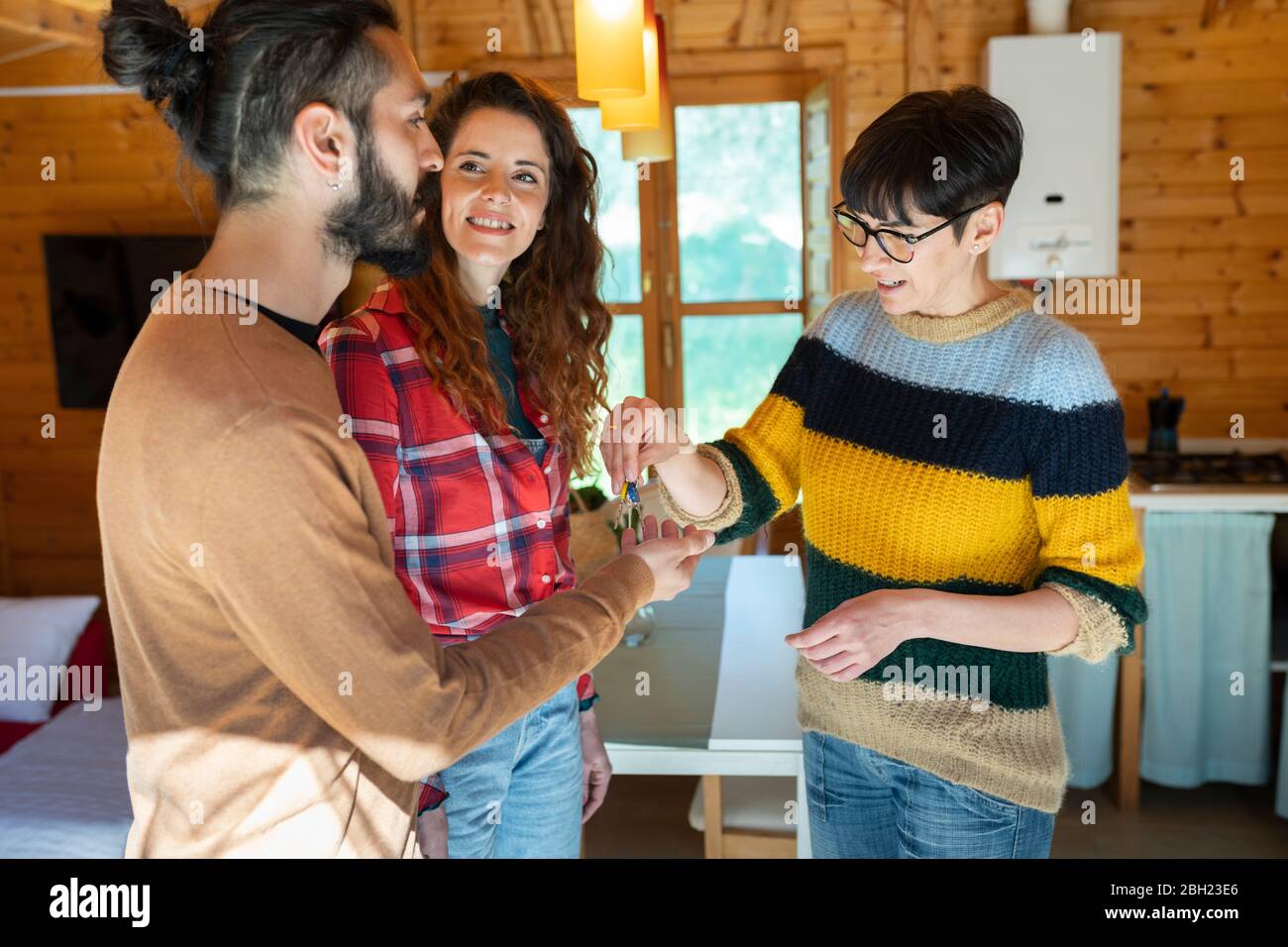 Gastgeber begrüßen junges Paar in einer Hütte auf dem Land Übergabe des Hausschlüssels Stockfoto