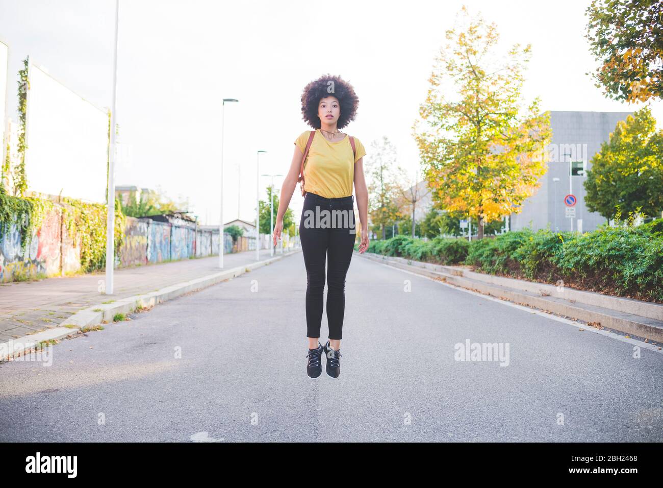 Junge Frau mit Afro-Frisur springt auf einer Straße in der Stadt Stockfoto